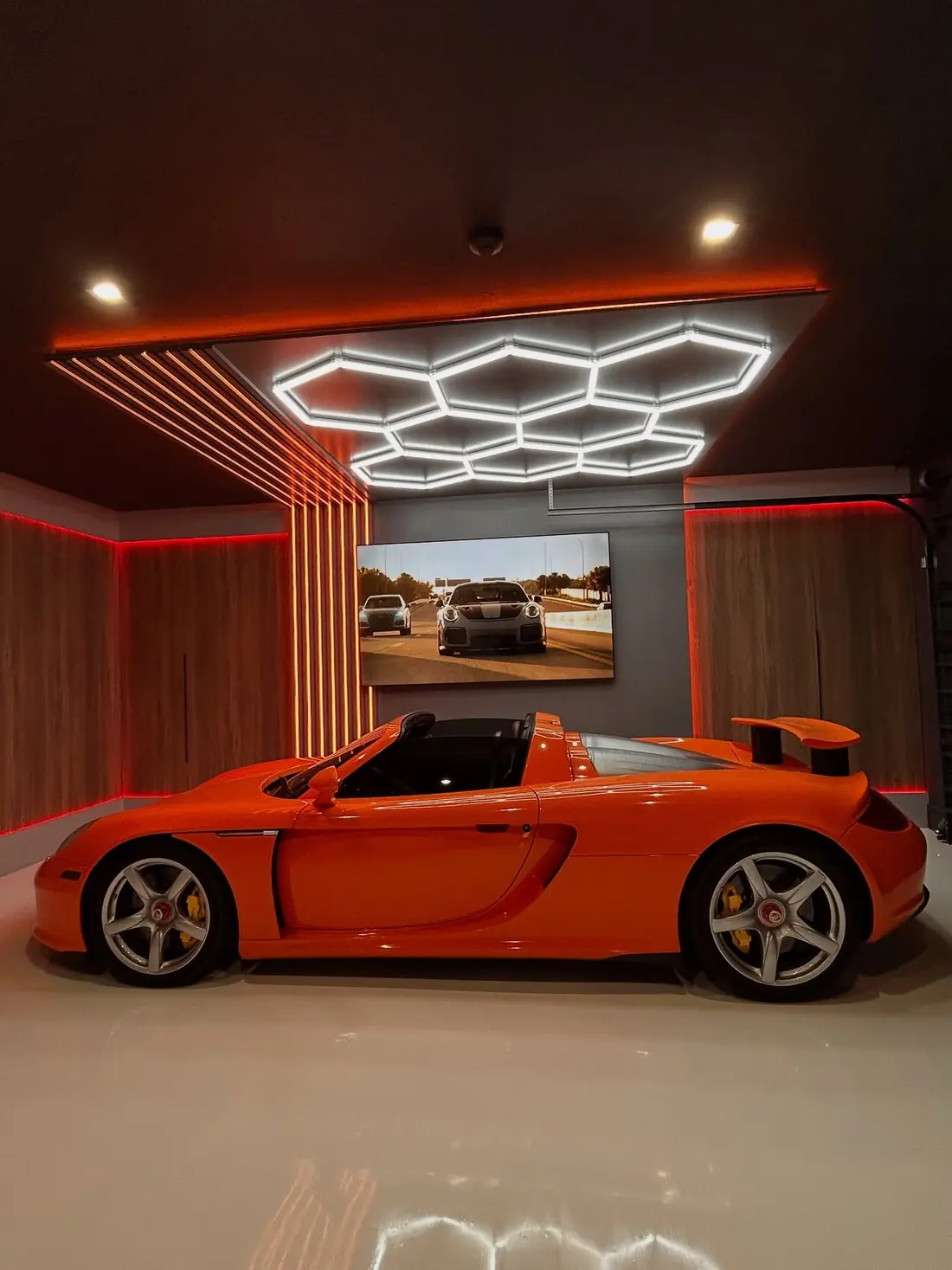 An orange Porsche Carrera GT under hexagon lights in Kamran's garage