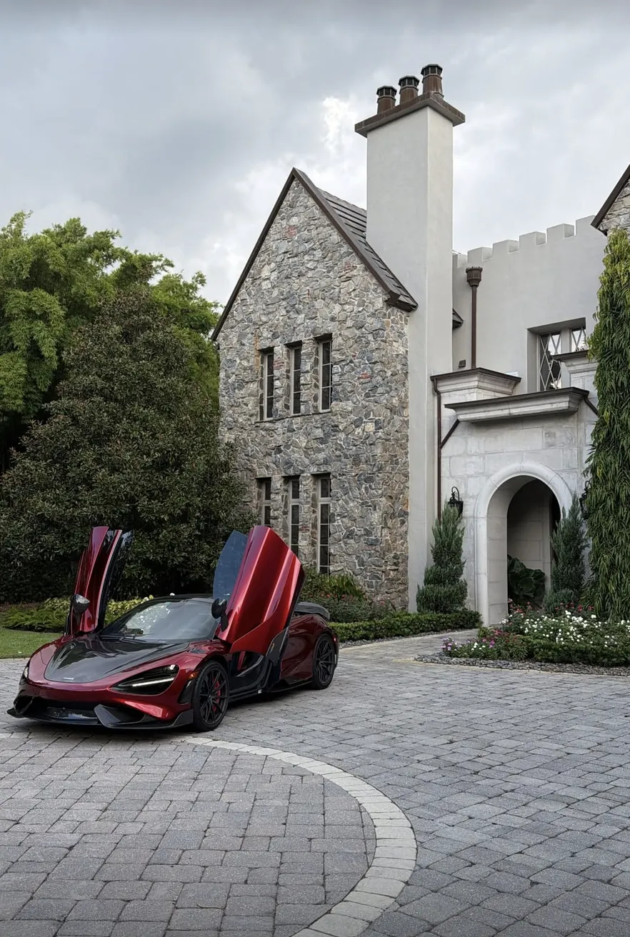 A red McLaren with its doors up outside a stone house